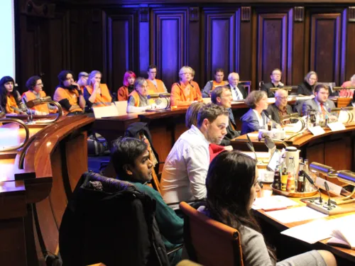 Etwa 16 Personen sitzen in zwei Reihen hinter Pulten im Hodlersaal des Neuen Rathauses.
